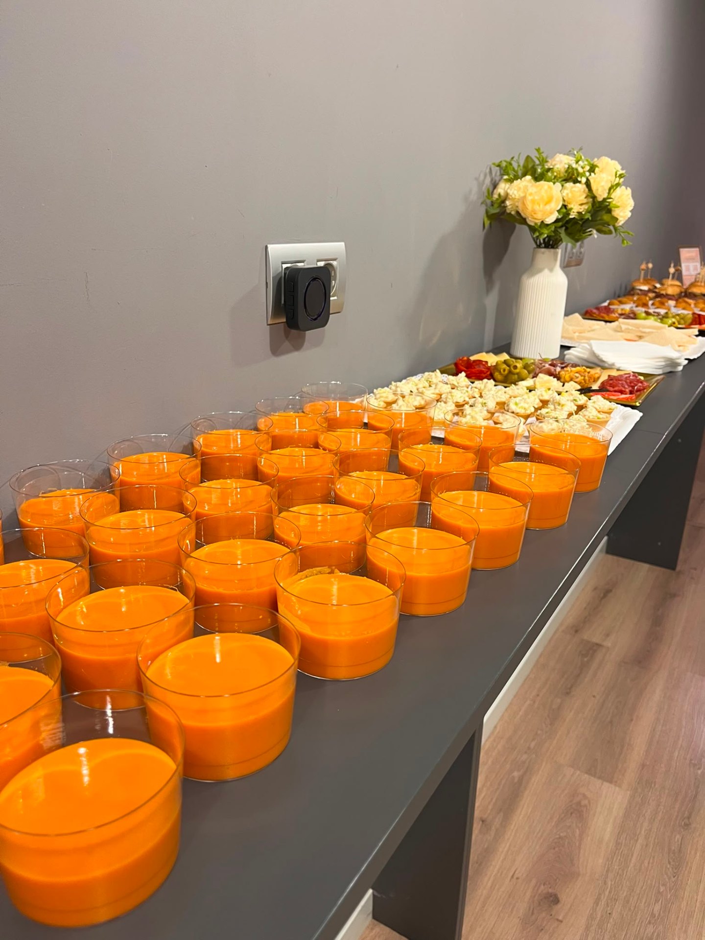 Mesa larga con vasitos de gazpacho y aperitivos